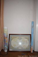 Photo of the lot with one framed world map leaning against wall, and two rolled maps standing upright