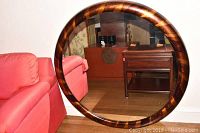 Mirror leaning against a wall next to red sofa, showing wooden striped frame and reflection of a room.