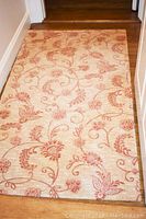 Full view of one matching wool rug showing beige background with rust floral vine pattern.