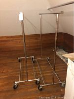 Two chrome metal rolling clothes racks positioned on wood floor with a wood-paneled wall background.