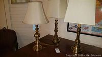 Three brass table lamps on a wooden table with beige shades, photographed to show overall size and design.