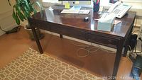 Desk viewed from the front showing top surface with items, three dovetailed drawers visible on front, polished dark brown finish.