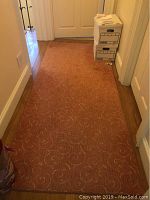 Photo of full coral area rug in hallway showing length and width with cream swirl design and minor wear.
