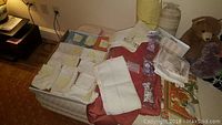Wide view of the linens and pillows arranged on a bed and chair, with napkins, table runner, twin sheet and pillows visible.