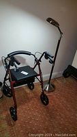 Side view showing the red mobility aid walker with padded handles and seat and the floor lamp with adjustable arm and metal base.