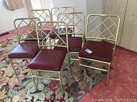 Six gold-tone steel frame banquet chairs with lattice backs and deep red leather seat cushions arranged on a patterned rug.