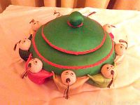 Top view of green silk pincushion with sewn children dolls around the rim