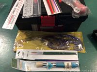 Top view showing paint brushes in packaging, transparent flexible artists' curves in original packaging, and the black toolbox underneath.