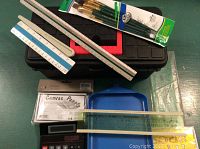 Photo showing the black plastic tool box with lift-out drawer, paint brushes, wooden and plastic rulers, a calculator, and plastic tray.
