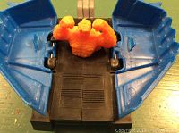 Close-up of blue plastic vehicle or container with an orange monster-like figure seated inside