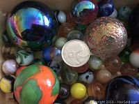 Close-up of assorted collector marbles in various sizes and colors with a quarter for size comparison.