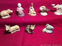 Front view of all 8 figurines arranged in two rows on red cloth background