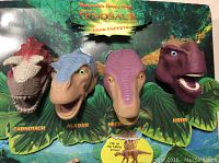 Four close-up dinosaur hand puppets on McDonald's store display showing names Carnotaur, Aladar, Neera, Kron