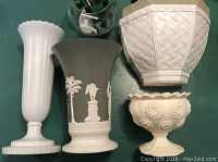 Four decorative white and grey vases including a tall white fluted vase, a grey classical style relief vase, a white basket-weave planter, and a small floral relief vase.