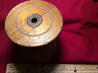 Top view of the antique wooden spool showing prominent crack and central metal ring, on red fabric background with a ruler to indicate size.