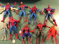 Multiple Spiderman and friend action figures in various poses and colors, some with string accessories on a green background.
