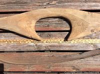 Close-up image of the carved wooden yoke showing the central oval opening and slits at ends with a measuring ruler beneath for scale.