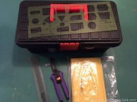 Photo showing a black and red plastic tool box with metal alphabet stencil placed on top, along with purple handled scissors and a metal ruler next to a plastic black stencil sheet.