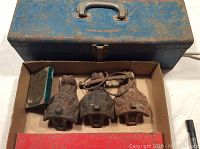 Blue metal toolbox with assorted rusted tools and a cardboard box holding three rusty iron bathtub feet