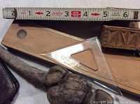 Close up of Lufkin wooden ruler with clear plastic 45° angle triangle and wood knurl, partial view of carved wooden box and leather wallet in background