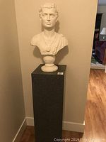 Full view of Julius Caesar bust on Corian pedestal against a beige wall with wooden floor visible