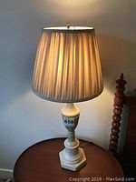 First matching plaster table lamp lit, showing pleated lampshade and carved base details.