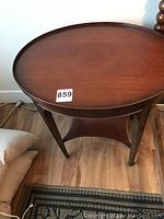 Oval mahogany end table top surface showing wood grain and slight imperfection at rim edge.