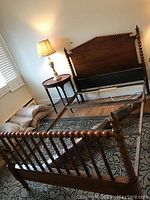 Full view of walnut bed frame assembled with twisted spindle posts and footboard visible along with headboard, adjacent furniture, and linens on floor.