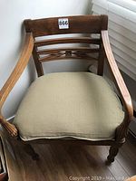 Full front view of the hand carved fruitwood chair with a beige cushion on the seat and curved armrests.