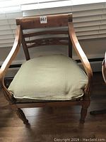 Front view showing chair with light removable cushion on cane seat and carved wooden frame with curved arms.