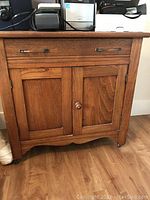 Front view of vintage elm wood cabinet showing one drawer with metal handles and two wood paneled doors with a round knob