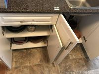 Photo of open kitchen cabinet with various bowls, pans, and containers stored inside showing general assortment of baking and kitchenware items.
