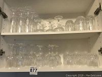 Shelf with various crystal stemware including wine glasses and champagne flutes, neatly arranged in rows.