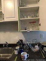 Clear glass cocktail glasses, shot glasses, and martini glasses with red rim displayed inside cabinet above sink.