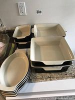View of stacked oval bowls and rectangular dishes showing beige interiors and black exteriors on a kitchen counter.