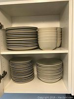 Stacked white dinner plates and bowls in a white cabinet shelf.