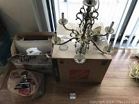 Photo of chandelier placed on cardboard boxes, showing all eight arms and attached candle-style bulb holders.
