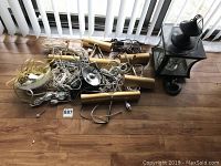 Photo of brass cylindrical art lights with cords and mounting brackets, along with large brass lantern light on a wood floor near window.