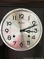 Close-up shot of the Brentwood clock dial showing the brand name, black Arabic numerals, ornate hands, and keyholes for winding the 31 day mechanical movement.
