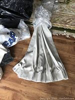 White or light-colored custom cut plastic blinds folded and tied together, laid on wooden floor with some bags nearby.