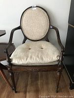 Front view of vintage fruitwood chair showing oval upholstered back with beige damask fabric and removable padded seat cushion with two buttons.