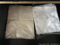 White folded linens, possibly larger tablecloths or sheets in plastic packaging
