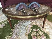 Oval coffee table with marble top and walnut legs shown on floral carpet.