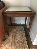 Front view of one walnut end table showing the mirrored top and wooden frame with gold floral detail on the corner.