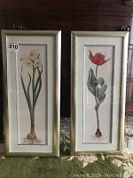 Two framed floral art prints displayed side by side against a dark wood chest. Each print is vertically oriented and has a silver frame with wide borders.