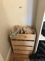 Wooden crate filled with multiple glass wine bottles, corking machine, and bag of corks on top.