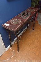 Full view of the narrow rectangular hall table with painted wood, gold inlaid lacquer top, and decorative black legs with gold motifs.