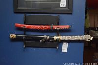Full view of the two swords displayed on the black wooden stand mounted on a blue wall