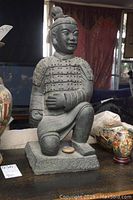 Frontal view of the 22 inch Asian style warrior statue on a table with various decorative items around.