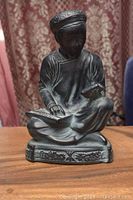 Front view of resin figurine showing person holding abacus on lap and scroll in hand, wearing hat and robe with ornate base.